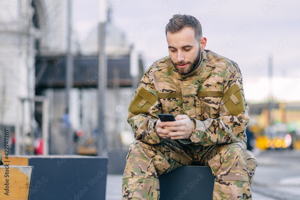 A military soldier sits on a bench at a bus stop waiting for a b A military soldier sits on a bench at a bus stop waiting for a b
