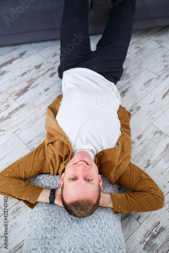 Happy young man lying on the floor near the sofa in the living room and resting © Дмитрий Ткачук