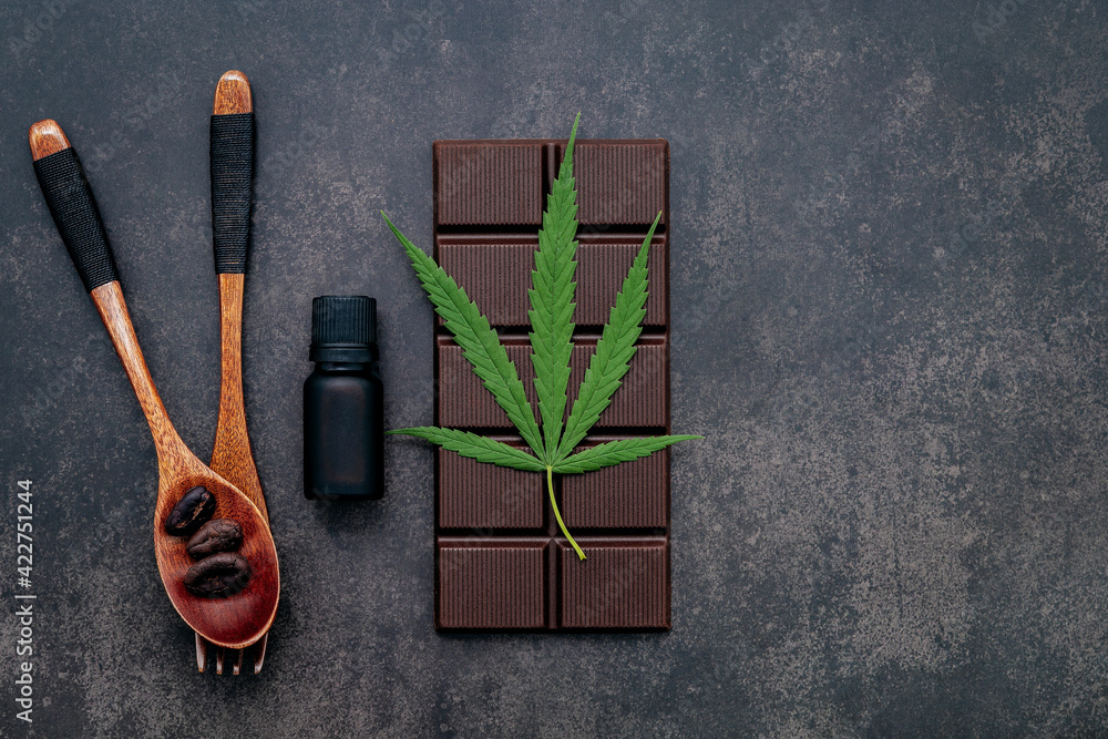 Food conceptual image of cannabis leaf with dark chocolate and fork on dark concrete background. Food conceptual image of cannabis leaf with dark chocolate and fork on dark concrete background.