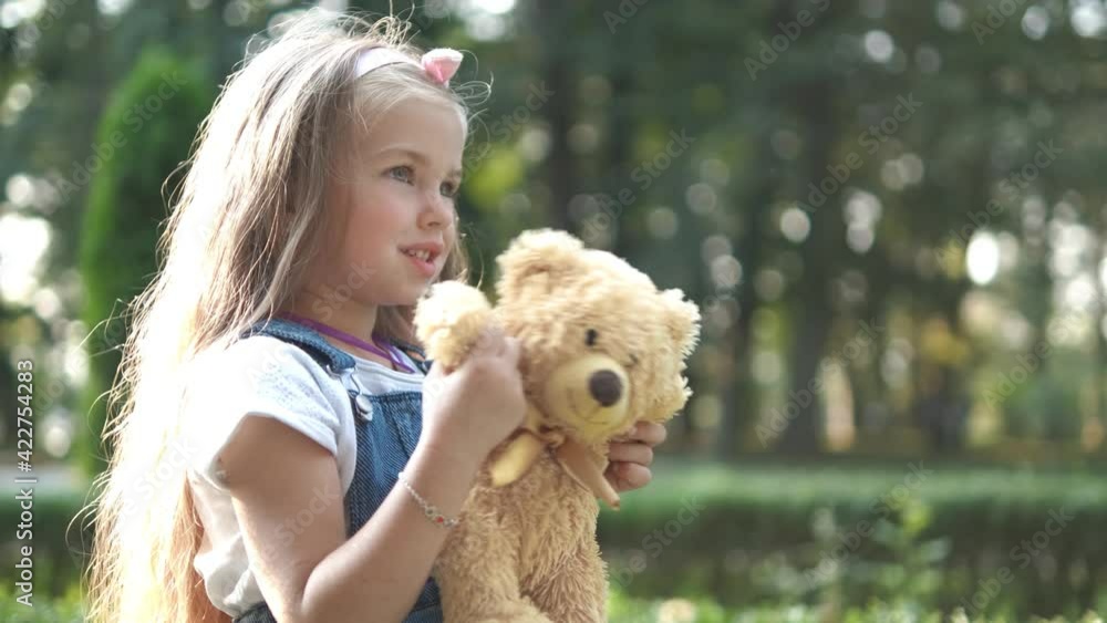 Pretty child girl playing with her favorite teddy bear toy outdoors in summer park. Pretty child girl playing with her favorite teddy bear toy outdoors in summer park.