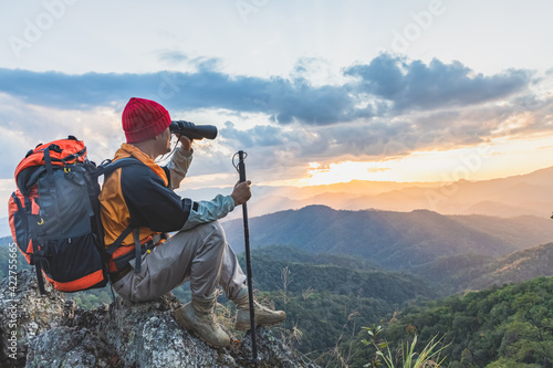 Hikers with backpacks holding binoculars sitting on top of the rock mountain photo
