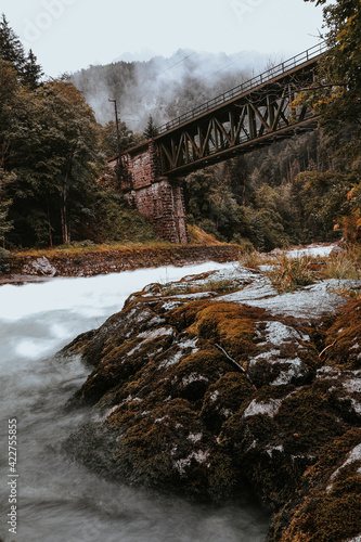 Ancient green railway bridge over wild river Enns in rainy weather in Gesause National Park near town of Admont in centre Austria. Long exposure emanates milk from water flowing along green nature photo