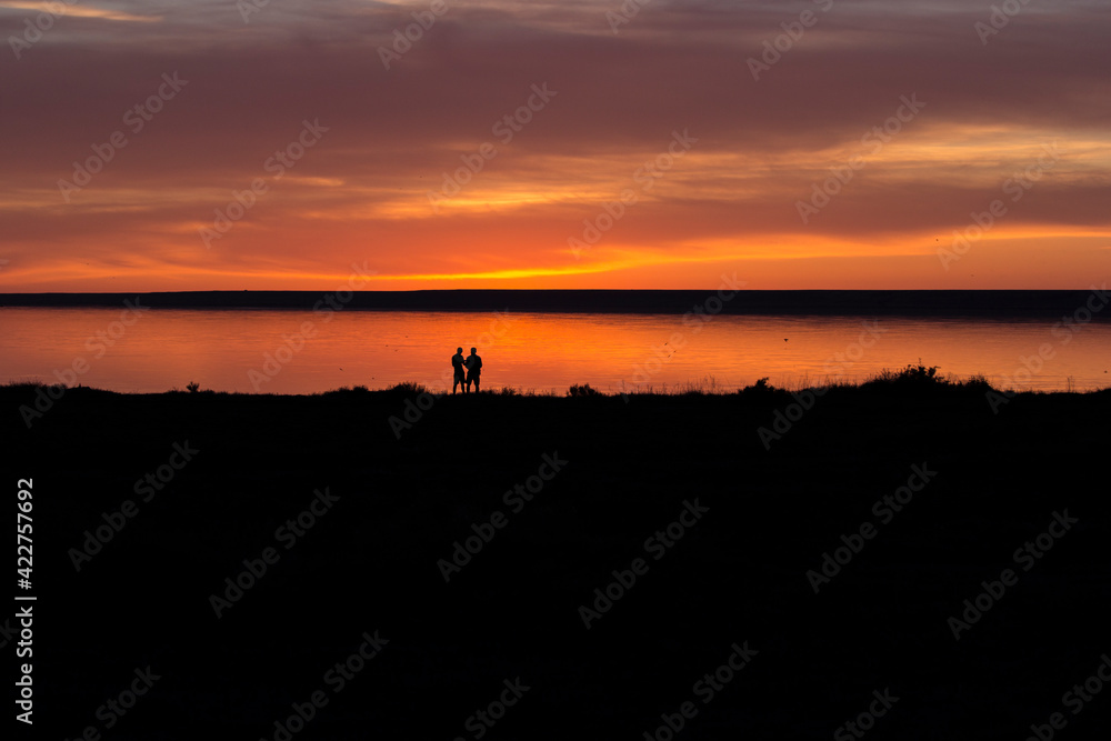 sunset by the lake, red tint and a silhouette of two people looking at a beautiful background