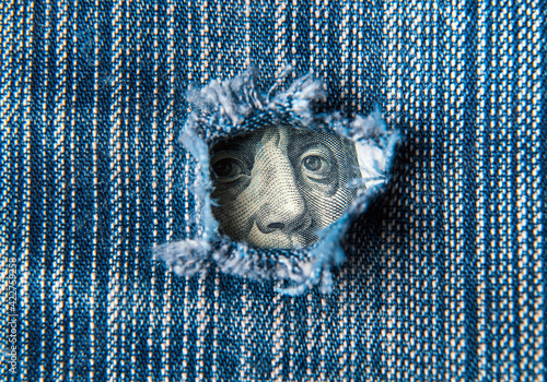 Hole in the pocket of denim pants from which dollars are visible. Symbolizes crisis or a hole in the economy. Falling financial profit