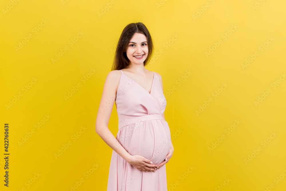 Happy pregnant woman touching her abdomen at Colored background. Future mother is wearing white underwear. Expecting of a baby. Copy space Happy pregnant woman touching her abdomen at Colored background. Future mother is wearing white underwear. Expecting of a baby. Copy space