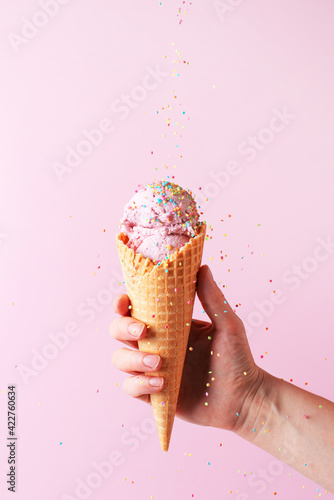 Female hand holding the pink ice cream with falling sprinkles in waffle cone