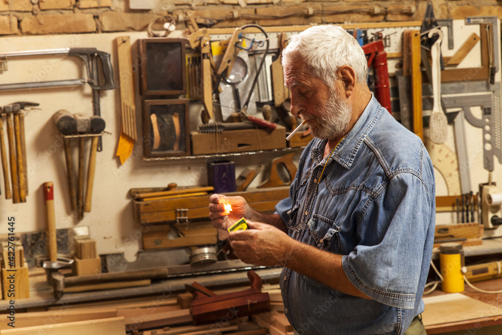 Senior carpenter taking a break and smoking in his workshop. Senior carpenter taking a break and smoking in his workshop.