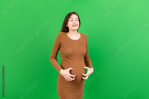 Pregnant woman scratching her belly on colored background