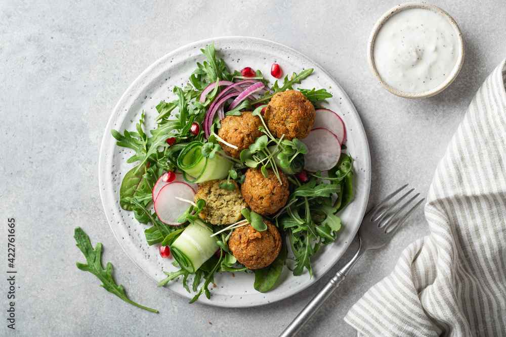 Falafel and fresh vegetables salad on a white ceramic plate on concrete background, top view. 