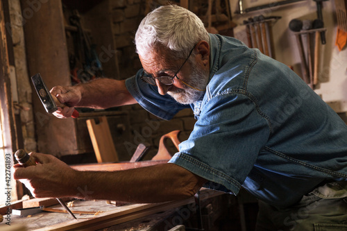 Experienced senior carpenter working in his vintage workshop.Carving and working with chisel. 