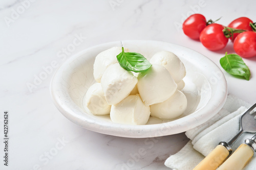 Mozzarella cheese with basil in white ceramic plate and tomato cherry on slate stone background, copy space. Mock up. Ingredients for Caprese salad.