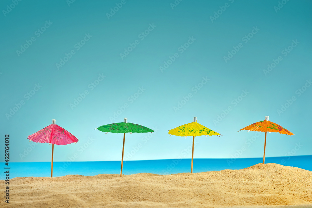 Beach umbrellas on the sand. Stylized cardboard beach. Paper umbrellas for cocktails in the background. The concept of rest, sea and vacation.