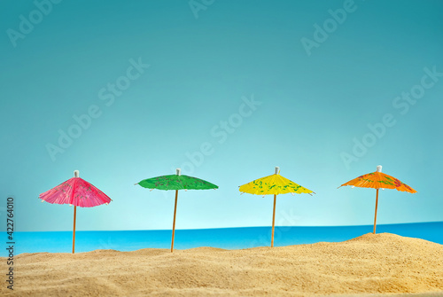 Beach umbrellas on the sand. Stylized cardboard beach. Paper umbrellas for cocktails in the background. The concept of rest  sea and vacation.