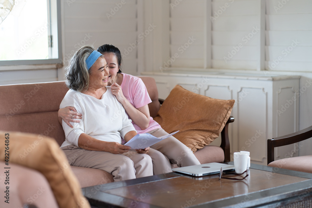 Cute Asian adult daughter embracing her mother with love in living room at home Cute Asian adult daughter embracing her mother with love in living room at home
