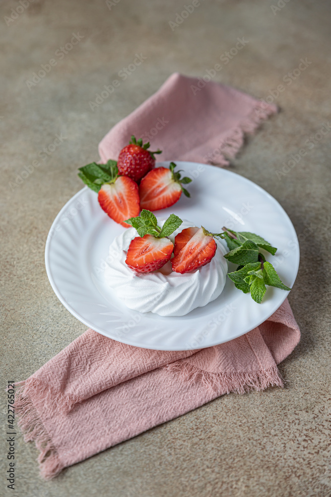 Mini Pavlova meringue cakes with strawberries and mint on a plate, concrete background.