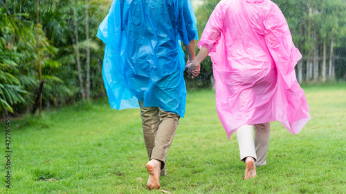 Happy Asian couple wearing a raincoat play in the rain outdoors at park.