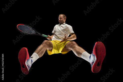 Young caucasian tennis player in action, motion isolated on black background, look from the bottom. Concept of sport, movement, energy and dynamic. © master1305