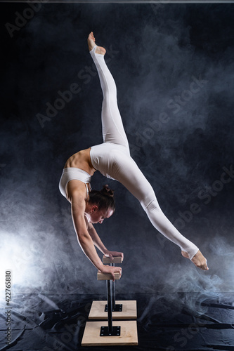 Flexible circus artist - female acrobat doing handstand on the back and smoker background. Concept of individuality and creativity