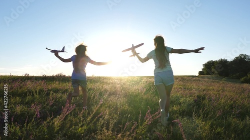 Silhouette of children playing on an airplane on a flower field. Dreams of flying. Happy childhood. Two girls play with a toy plane at sunset. Children on background of sun with an airplane in hand. photo