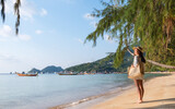 Portrait image of a beautiful young asian woman with hat and bag strolling on the beach