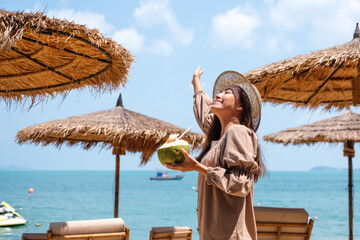 Portrait image of a beautiful asian woman holding a fresh coconut and enjoying on the beach