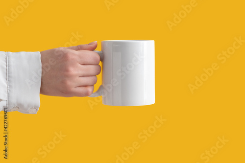 mockup ceramic white coffe cup or mug in female hands on yellow background with copy space. Blank template for your design, branding, business. Real photo. Woman in shirt casual style