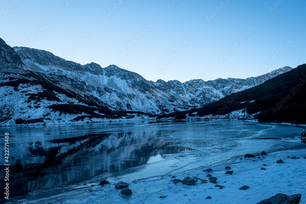 Shadows in the valley in Tatra Mountains, Poland. Sunny morning and the mountain ridge covering the sunlight. Selective focus on the rocks, blurred background.