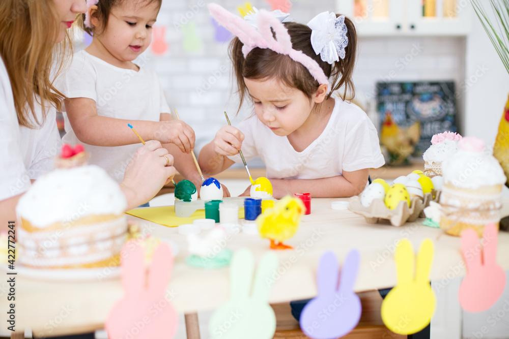 Two girls with bunny ears in the kitchen are decorating eggs for Easter. Easter holiday Two girls with bunny ears in the kitchen are decorating eggs for Easter. Easter holiday