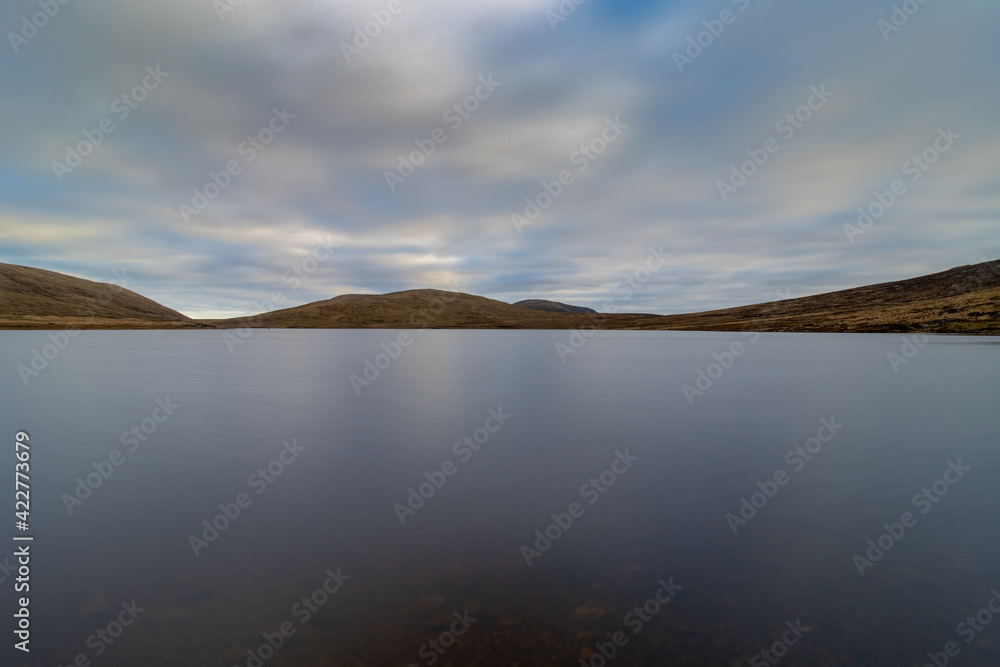 Spelga Dam, water reservoir in the Mourne Mountains. Clouds reflection on the lake with mountains on the background, long exposure. Spelga Dam, water reservoir in the Mourne Mountains. Clouds reflection on the lake with mountains on the background, long exposure.