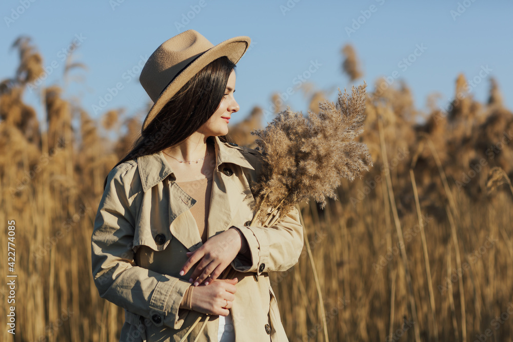 A girl dressed in neutral beige clothes on the field with dry reeds holds in her hands a reed bouquet. A girl dressed in neutral beige clothes on the field with dry reeds holds in her hands a reed bouquet.