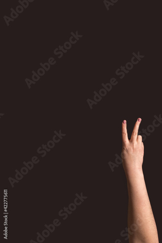 Hand showing "peace" sign. Two fingers raised on the black background. Vertical image with copy space.