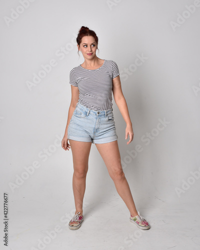 full length  portrait of girl wearing shirt and denim shorts. Standing pose isolated on grey studio background. photo