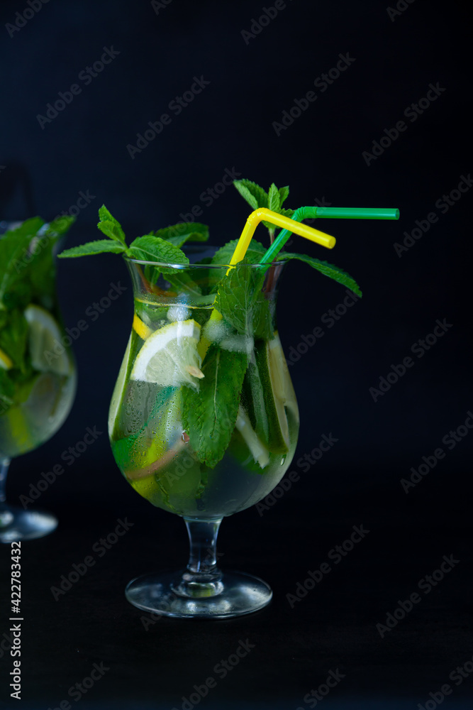 Summer mint lime refreshing cocktail mojito with rum and ice in glass on black background. Mojito cocktail on dark stone table. Glassy high glass for drinks. Lemonade at the bar. Summer mint lime refreshing cocktail mojito with rum and ice in glass on black background. Mojito cocktail on dark stone table. Glassy high glass for drinks. Lemonade at the bar.