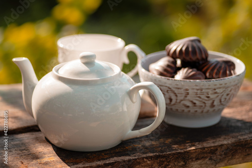 Teapot, marshmallow in chocolate, wooden table. Outdoor breakfast, picnic, brunch, spring mood. Soft focus