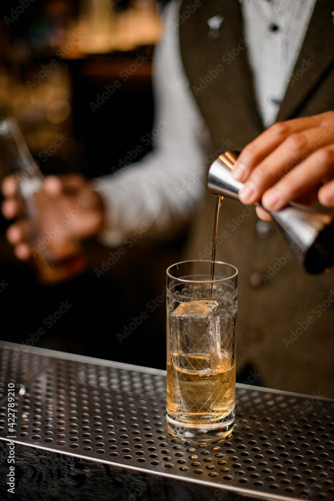 bartender holds steel jigger and pours beverage to glass with ice