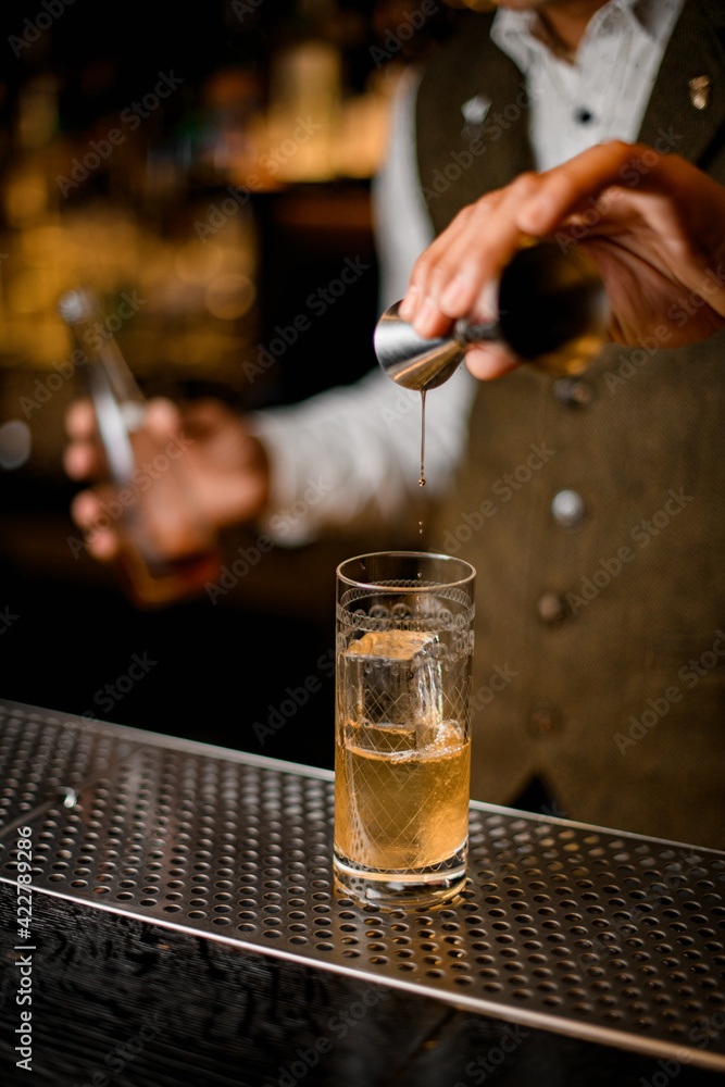 bartender holds steel jigger and gently pours beverage to glass with ice
