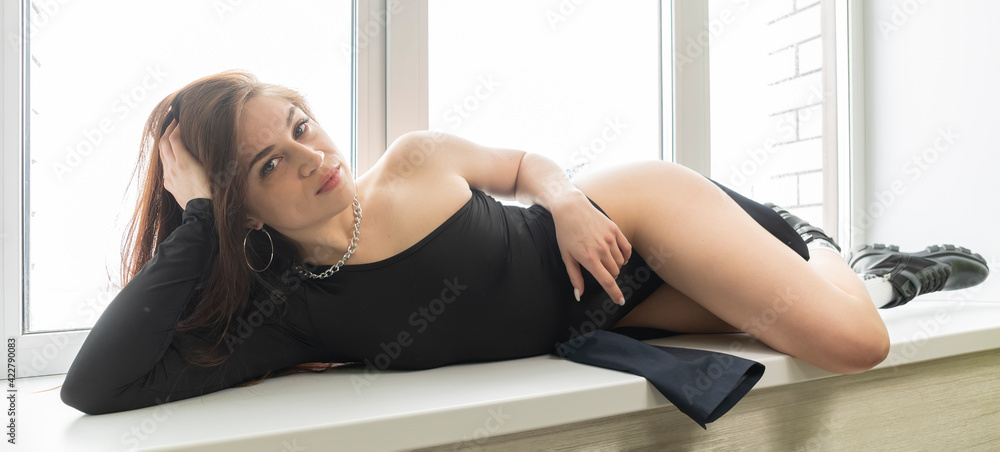 beautiful sexy woman in a black dress having fun relaxing lying on window  sill on light Stock-Foto | Adobe Stock