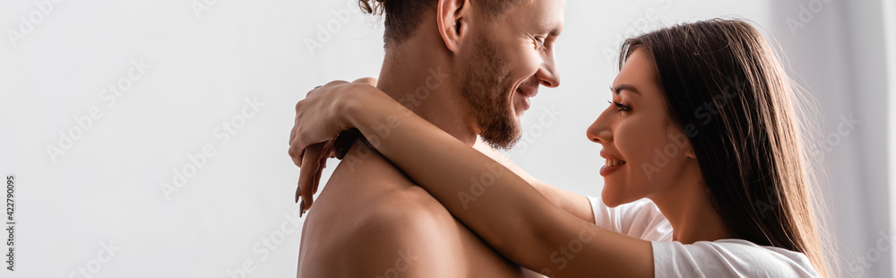 Side view of smiling woman hugging shirtless boyfriend at home, banner Side view of smiling woman hugging shirtless boyfriend at home, banner