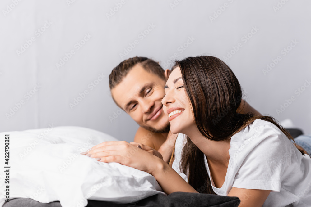 Smiling woman lying near shirtless man on bed on blurred background Smiling woman lying near shirtless man on bed on blurred background