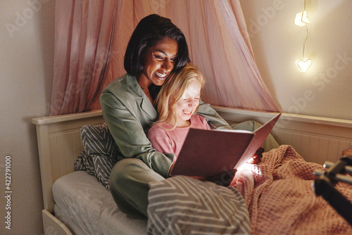 Laughing mom and her little girl reading a bedtime story