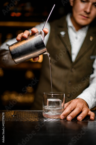 bartender pours drink from steel mixing cup with strainer into old-fashioned glass with ice