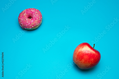 Donut and apple on the blue background. Choosing between apple and donut. Healthy lifestyle or nutrition concept. Dilemma between healthy good fresh fruit and sweets with a lot of sugar and calories.