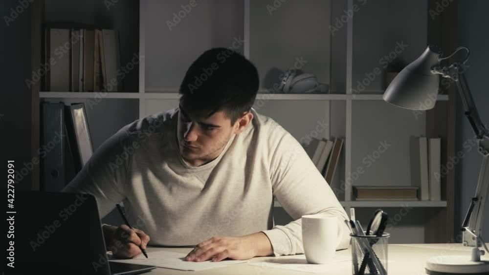 Night learning online. Internet meeting. Distance education. Smart male student working late at virtual class using laptop listening watching video lesson writing taking notes at dark workplace. Night learning online. Internet meeting. Distance education. Smart male student working late at virtual class using laptop listening watching video lesson writing taking notes at dark workplace.
