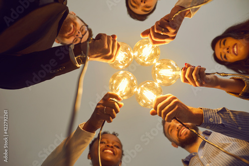Bottom view of interracial colleagues stacking together light bulbs as a symbol of a new business idea. Concept of sharing ideas, business, teamwork and brainstorming. Selective focus.
