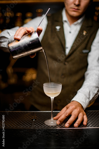 view of bartender gently pouring drink from mixing cup with strainer