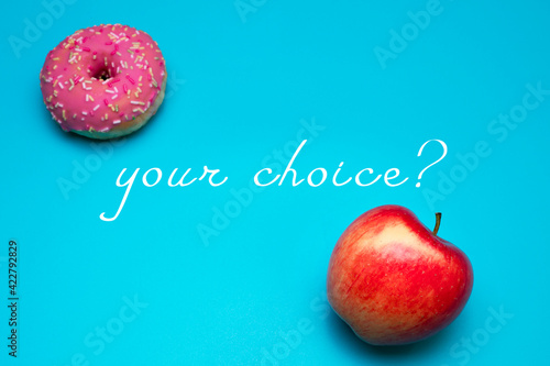 Donut and apple on the blue background. Choosing between apple and donut. Healthy lifestyle or nutrition concept. Dilemma between healthy good fresh fruit and sweets with a lot of sugar and calories. photo