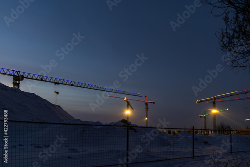 illuminated construction cranes at a construction site against the night sky