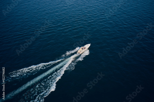 Yacht in the rays of the sun on blue water.  Aerial view luxury motor boat. Drone view of a boat sailing. Large speed boat moving at high speed side view. Travel - image. © Berg