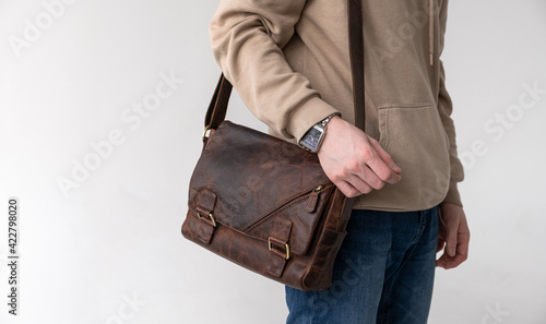 A young guy with a bag made of brown craft leather on a light background