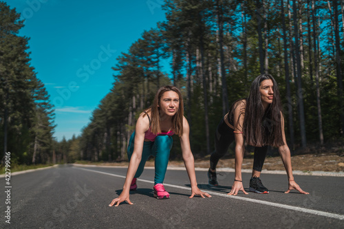 Fit female runners ready to go in a challenge outdoors on an asphalt road © mihail